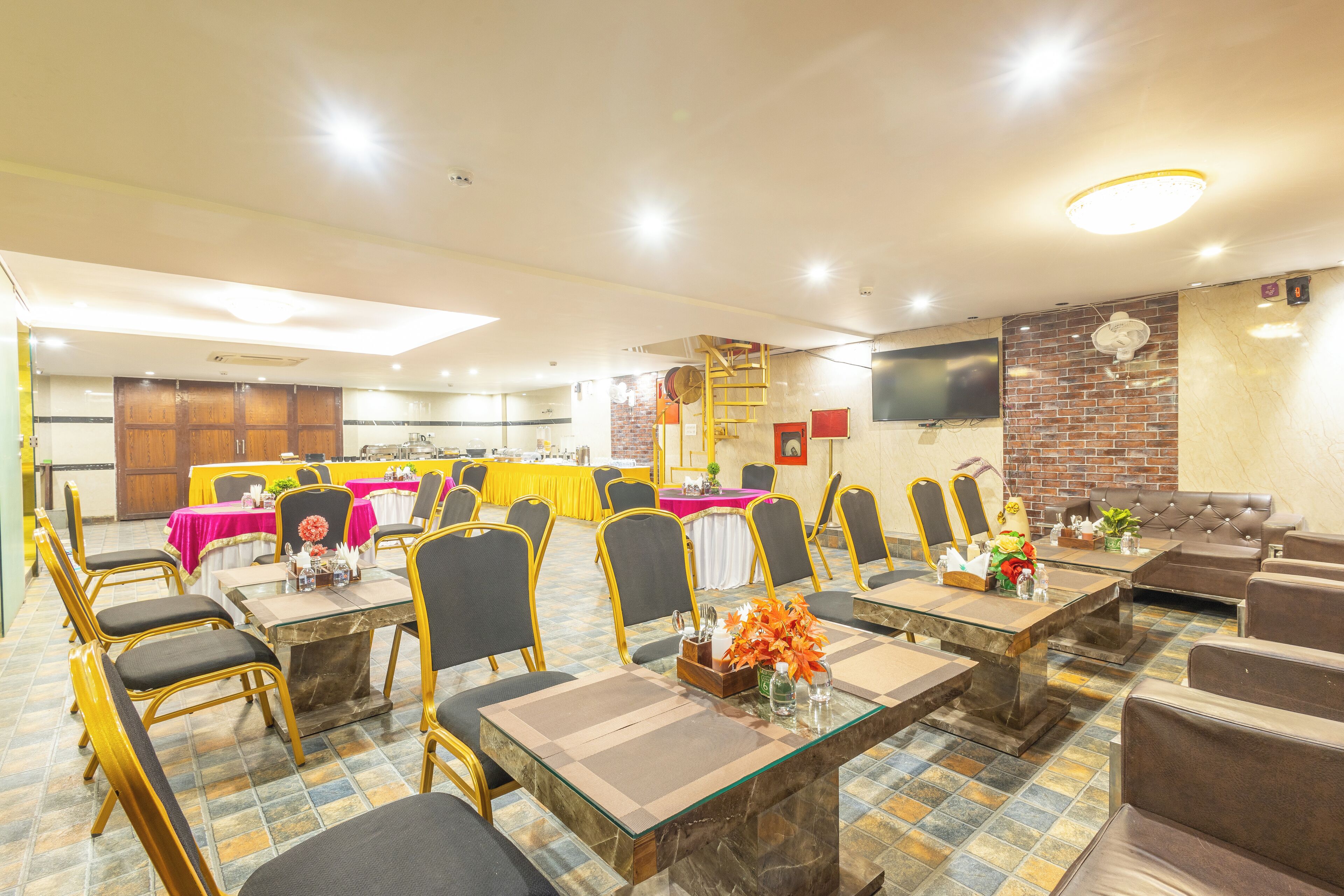 A dining area with tables and chairs, a brick wall, and a television on the wall.