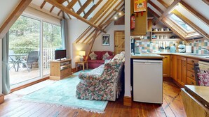 A loft-style room with a wooden ceiling, a sofa, a television, a kitchen area, and a sliding glass door leading to an outdoor patio. - Little Hanger, Porlock (Porlock)
