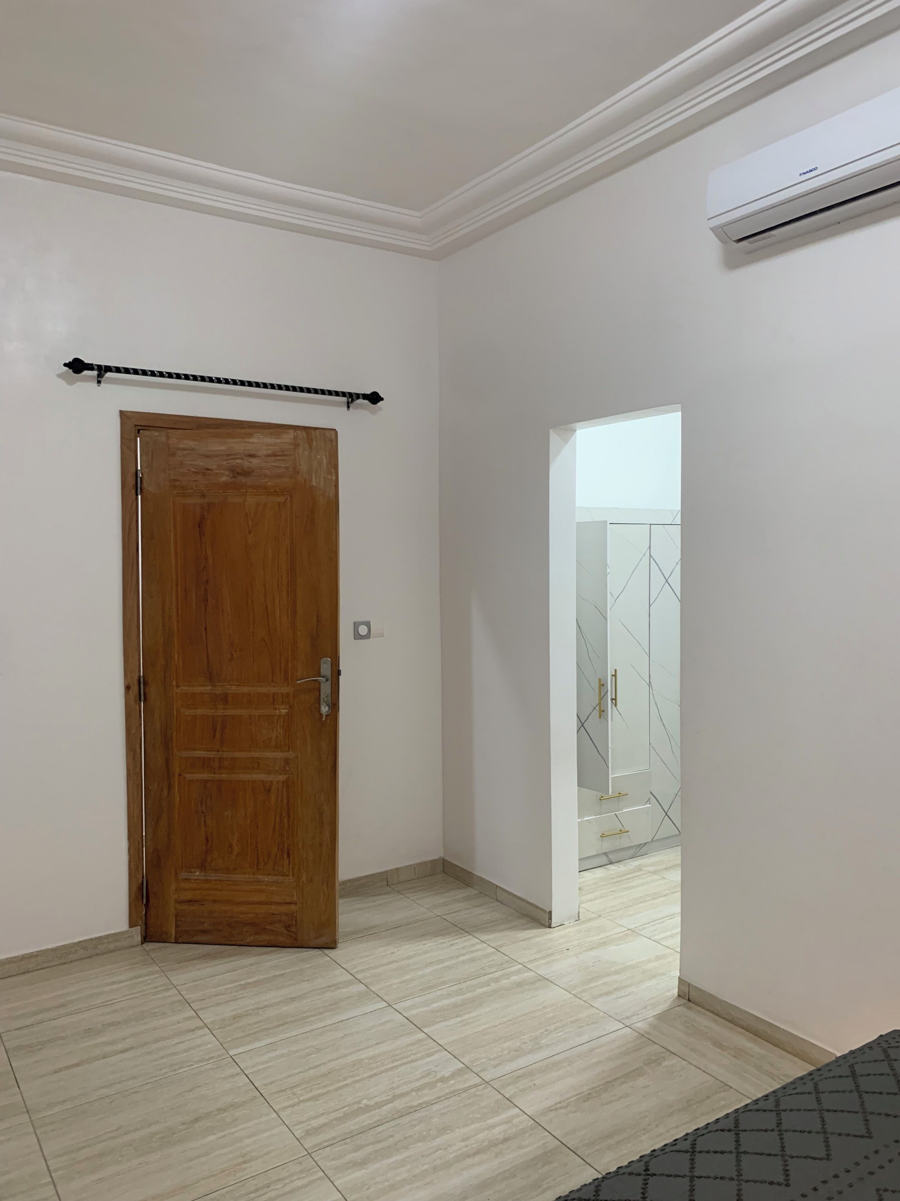 A room with a wooden door, a ceiling-mounted air conditioner, and a tiled floor.