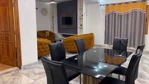 A dining area with a glass table and black chairs, a yellow sofa, and a grey curtain.