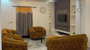 A modern living room with a sofa set, a flat-screen TV, and a chandelier.