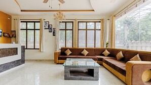 A modern living room with a sectional sofa, a glass coffee table, and large windows with curtains. - The Tiger Heritage  (Sawai Madhopur)