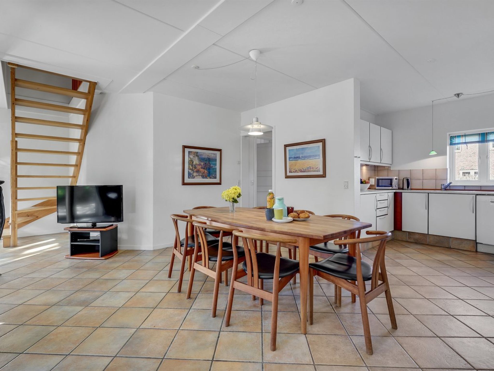 Ein Essbereich mit Holztisch, Stühlen, einem Fernseher und Bildern an der Wand.