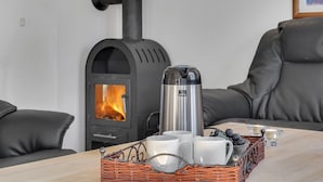 Una habitación acogedora con una estufa de leña, una cafetera y una cesta de mimbre con tazas y uvas.