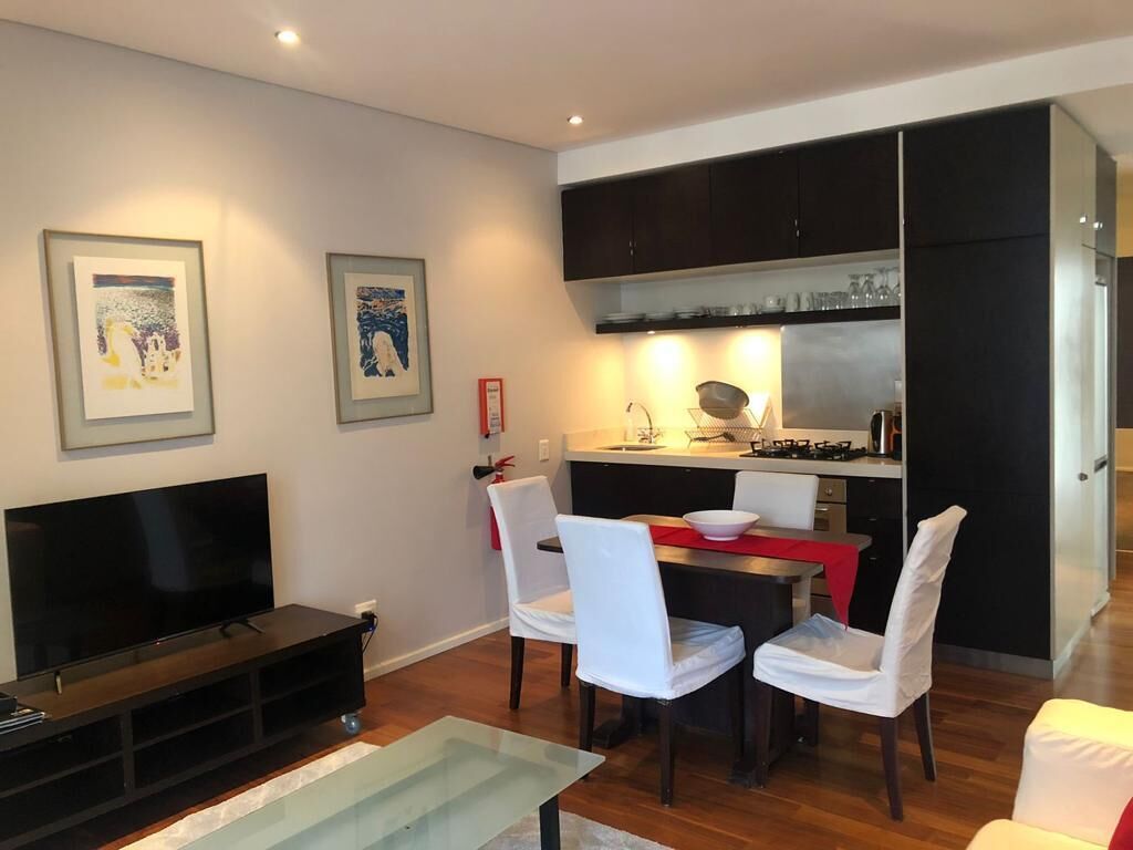 Un salon moderne doté d’un téléviseur à écran plat, d’une table à manger avec des chaises et d’un coin cuisine avec des placards et des appareils électroménagers.