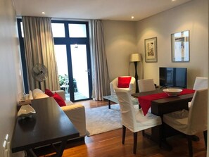 A modern hotel room with a dining area, a TV, and a large window with curtains. - Loader Street Apartment - Lovely one Bedroom in De Waterkant (Cape Town)