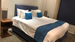 Ein ordentlich bezogenes Bett mit weißer und blauer Bettwäsche, ein Nachttisch mit Lampe und ein dunkelblaues Kopfteil.