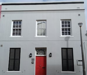 Un edificio con tre finestre al piano superiore, una porta rossa con un pannello di vetro decorativo e persiane al piano inferiore.