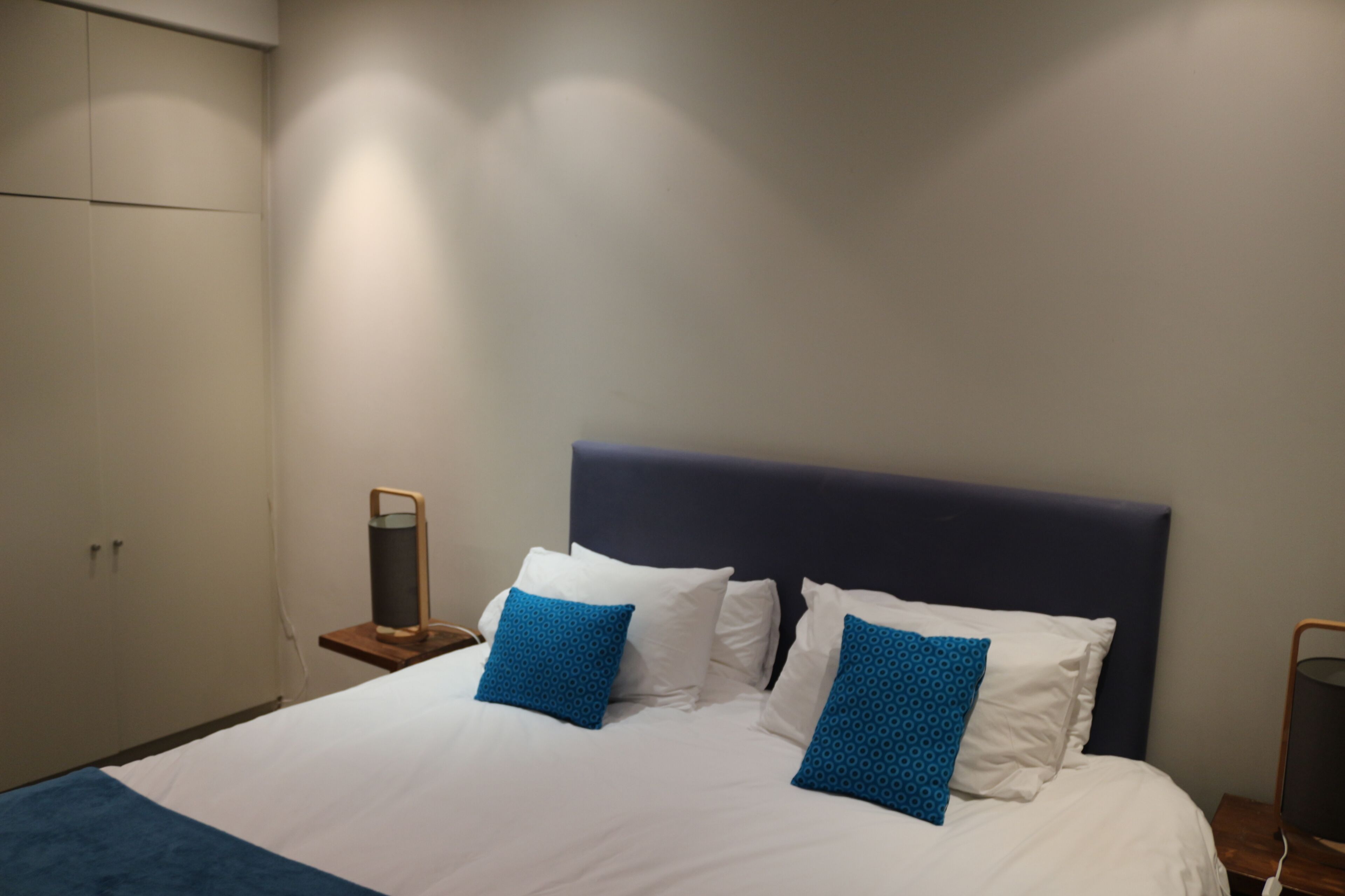 A neatly made bed with white and blue pillows, a dark headboard, and a bedside table with a lamp.