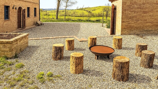 A courtyard with a gravel ground, wooden stumps, and a fire pit.