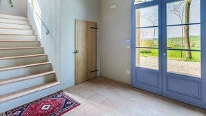 A staircase leading to a wooden door, a blue door with a view of greenery, and a patterned rug on the floor.