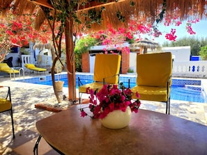 A poolside area with a table, yellow chairs, and a vase of pink flowers.