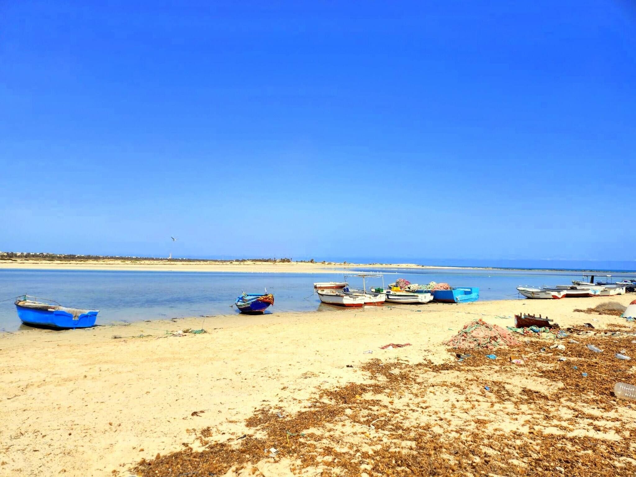 A beach with several boats anchored near the shore, a sandy beach, and a clear blue sky.