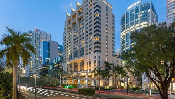 A JW Marriott hotel with a modern design, surrounded by palm trees and other buildings.