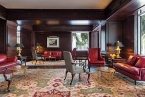 Un salon spacieux avec des canapés en cuir, une moquette à motifs et une grande fenêtre donnant sur des palmiers.