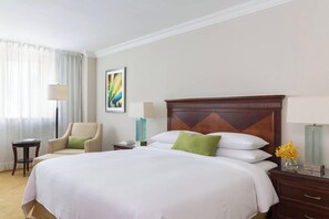 Une chambre d’hôtel avec un grand lit, une chaise, une table de chevet, une lampe et un vase rempli de fleurs.