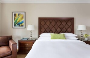 Una habitación de hotel con una cama grande, dos mesitas de noche con lámparas, una silla y un cuadro abstracto enmarcado en la pared.