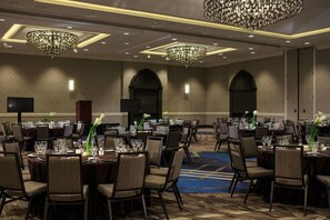 A conference room with round tables, chairs, and chandeliers.