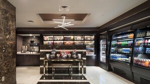 A modern lobby with a marble floor, a central seating area, and vending machines stocked with snacks and beverages.