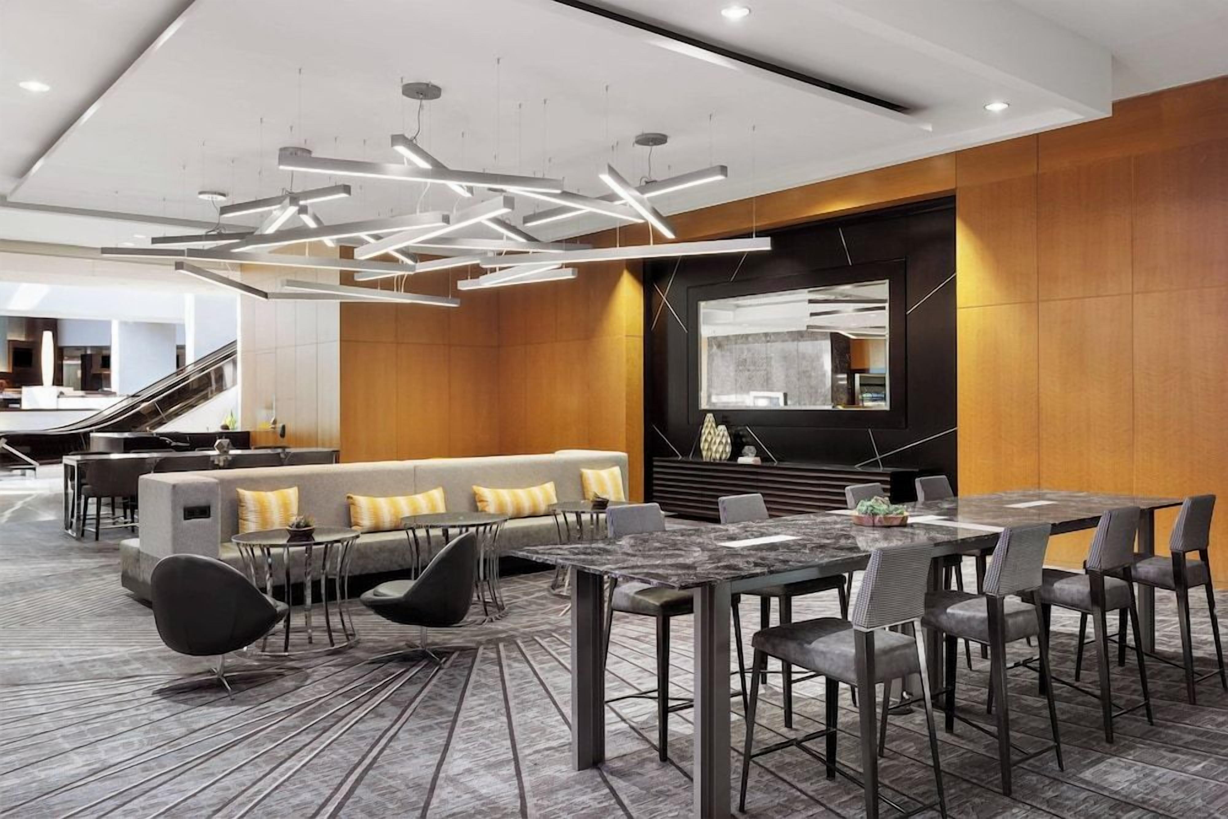 A modern hotel lobby with a central seating area, a dining table, and a staircase.