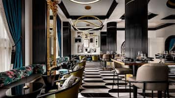 A modern interior with a black and white patterned floor, a seating area with sofas and armchairs, and a bar area with tables and chairs.