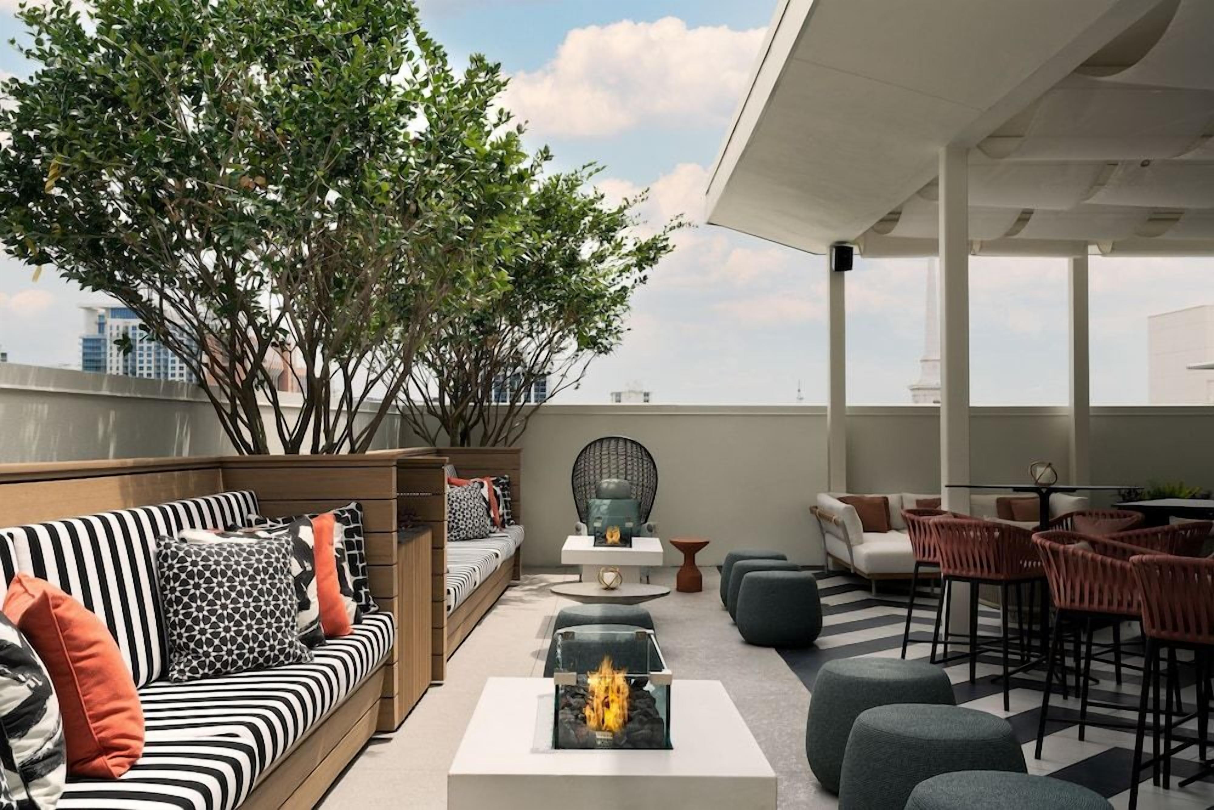 A rooftop lounge with a fire feature, seating arrangements, and a view of the city skyline.