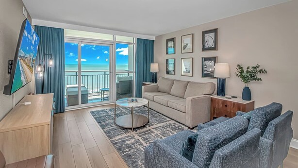 A modern living room with a sofa, coffee table, and TV. It features a balcony with a view of the ocean. - 1BR Direct Ocean Front Suite Newly Renovated! (Myrtle Beach)