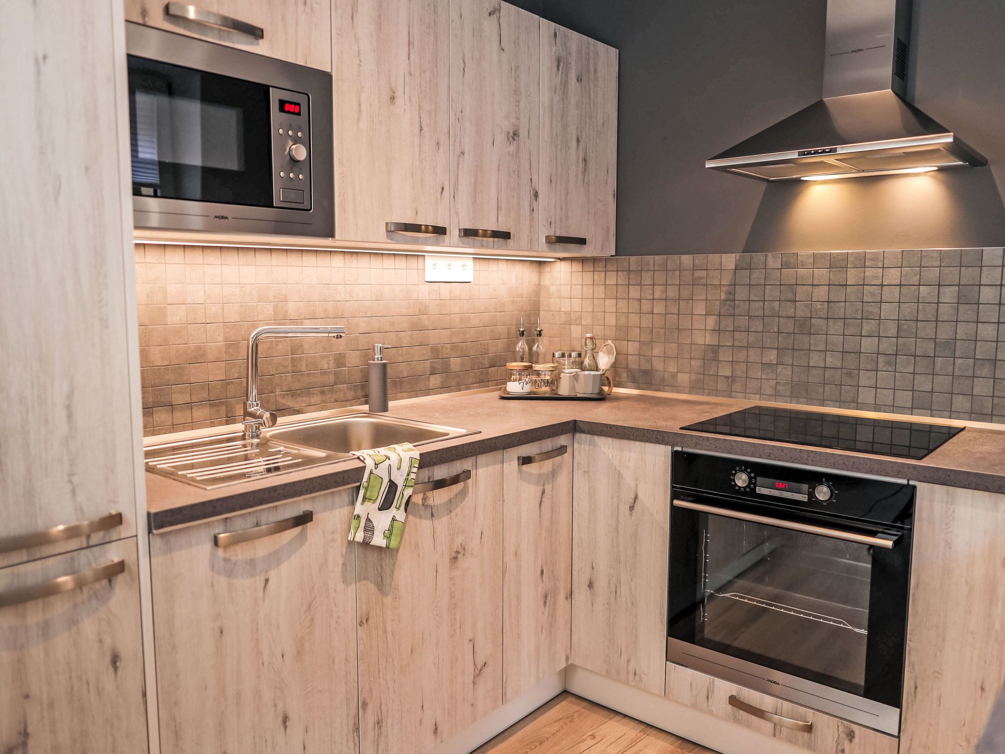Eine moderne Küche mit Holzschränken, einer Edelstahl-Mikrowelle, einem Backofen, einem Spülbecken mit Armatur und einer Kaffeemaschine.