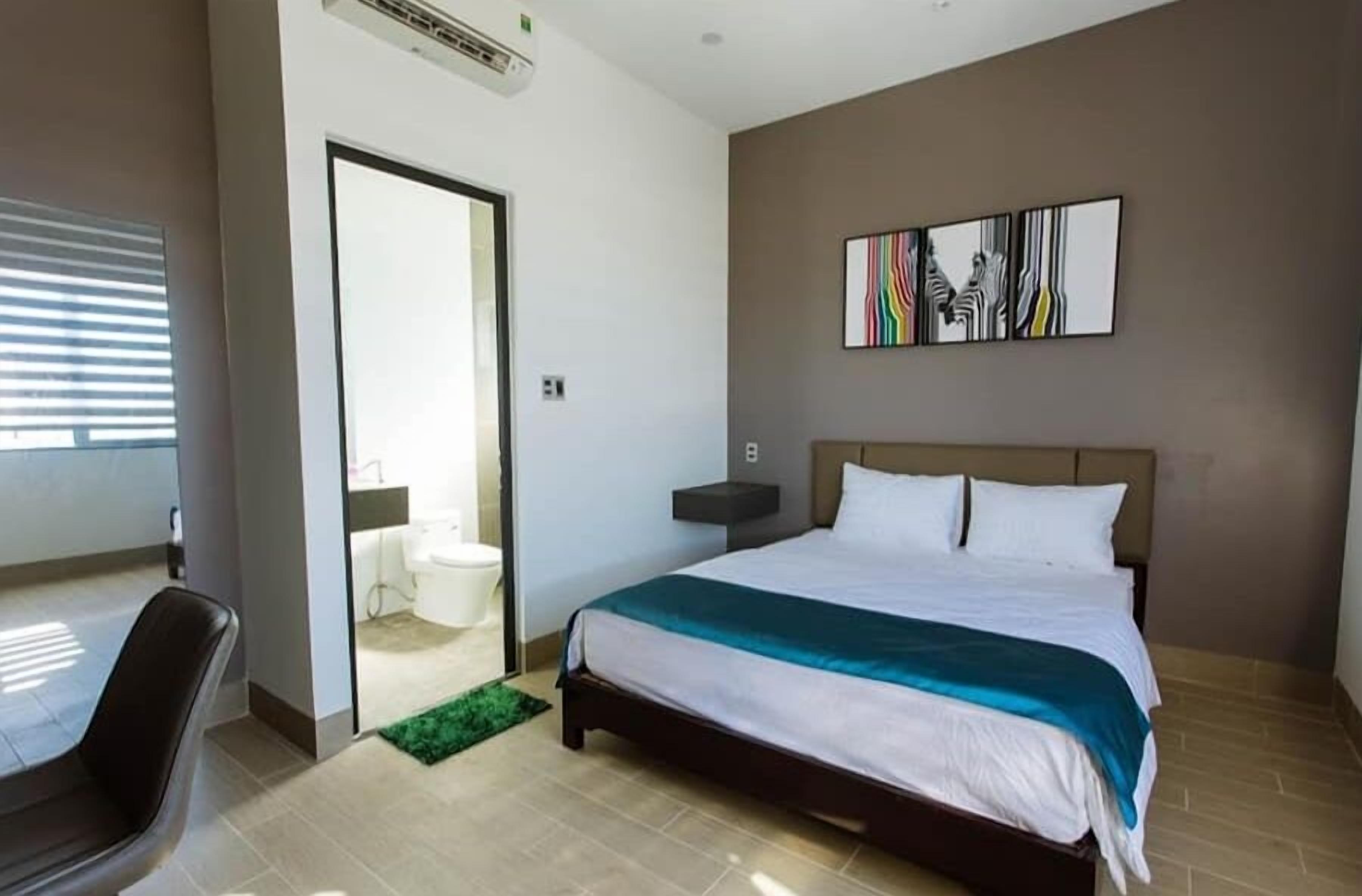 A modern hotel room with a large bed, a desk, and a bathroom visible through an open door.