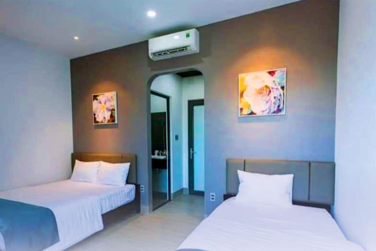 Habitación de hotel con dos camas individuales, un armario, una puerta que da al baño y un equipo de aire acondicionado en la pared.