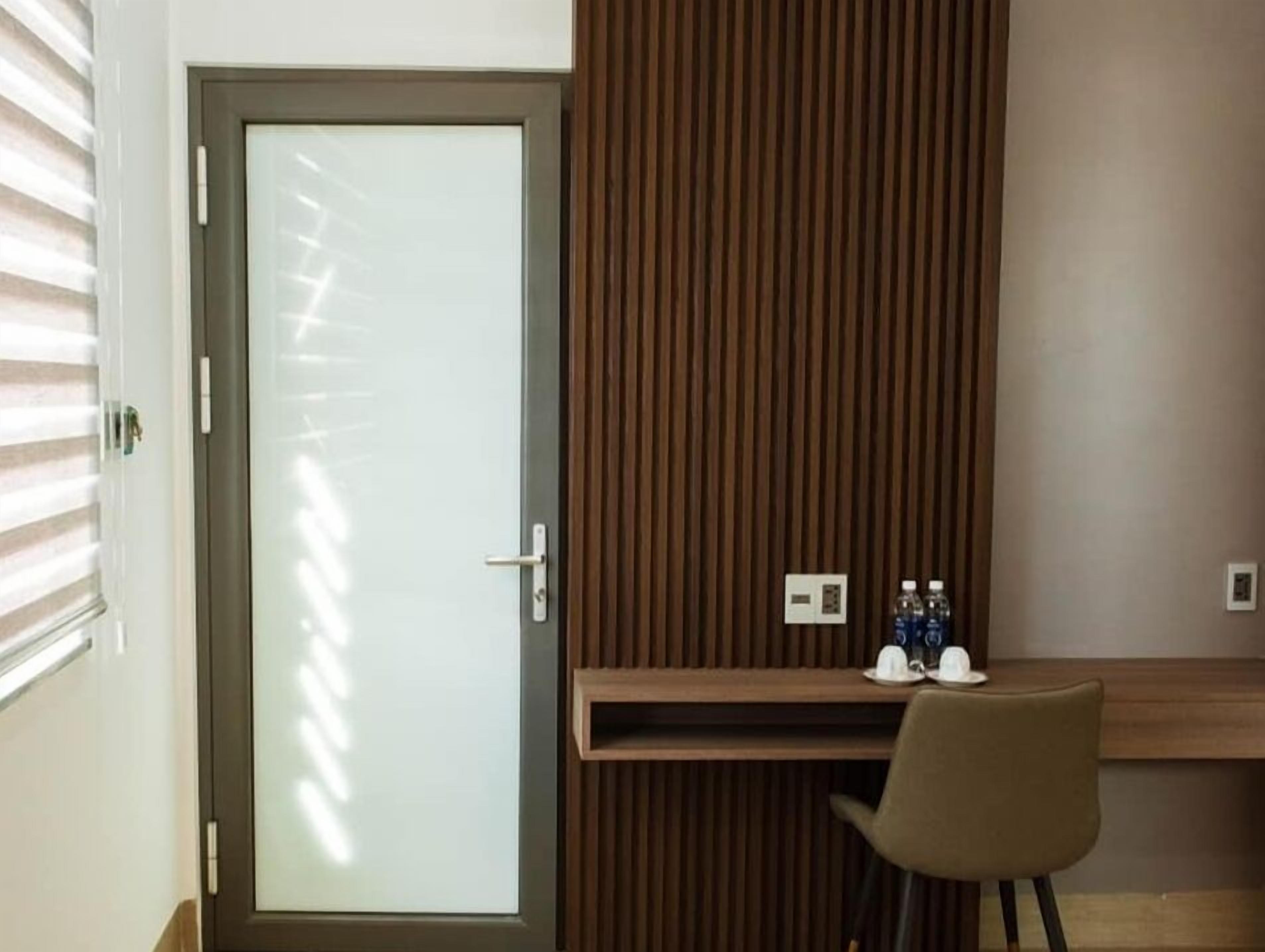 A hotel room with a wooden panel wall, a desk with two water bottles, and a chair.