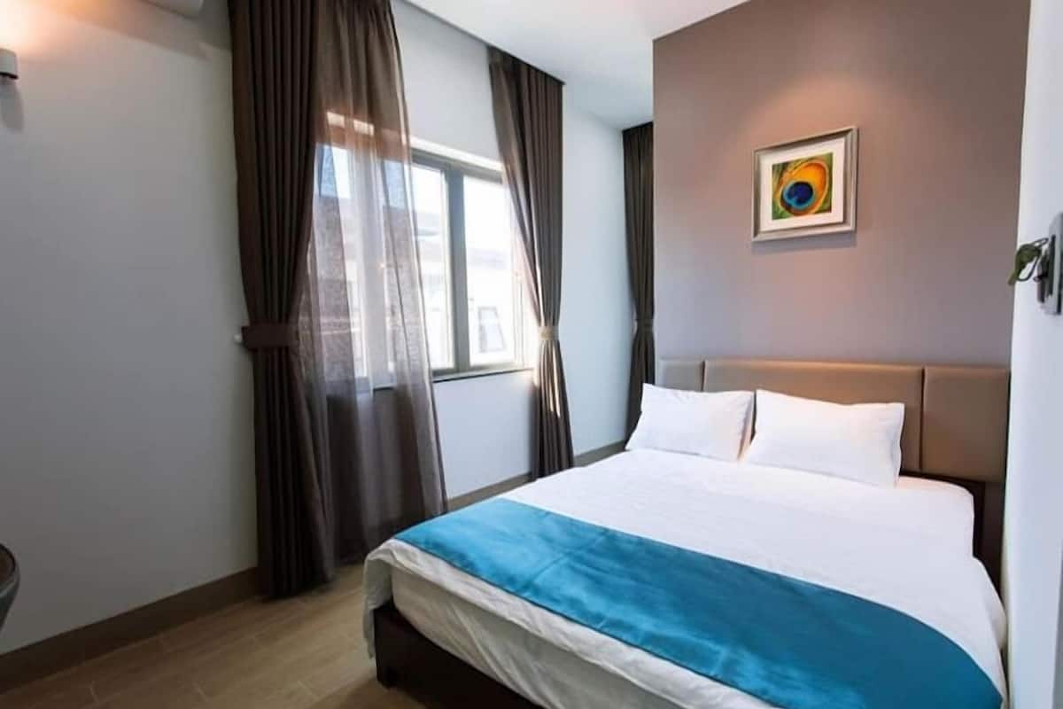Una habitación de hotel con cama, cortinas, una ventana y un cuadro colgado en la pared.