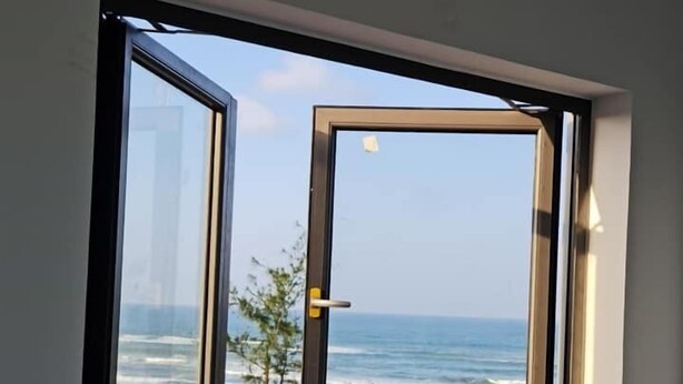 Una finestra amb vista a l'oceà i la vegetació de la platja.