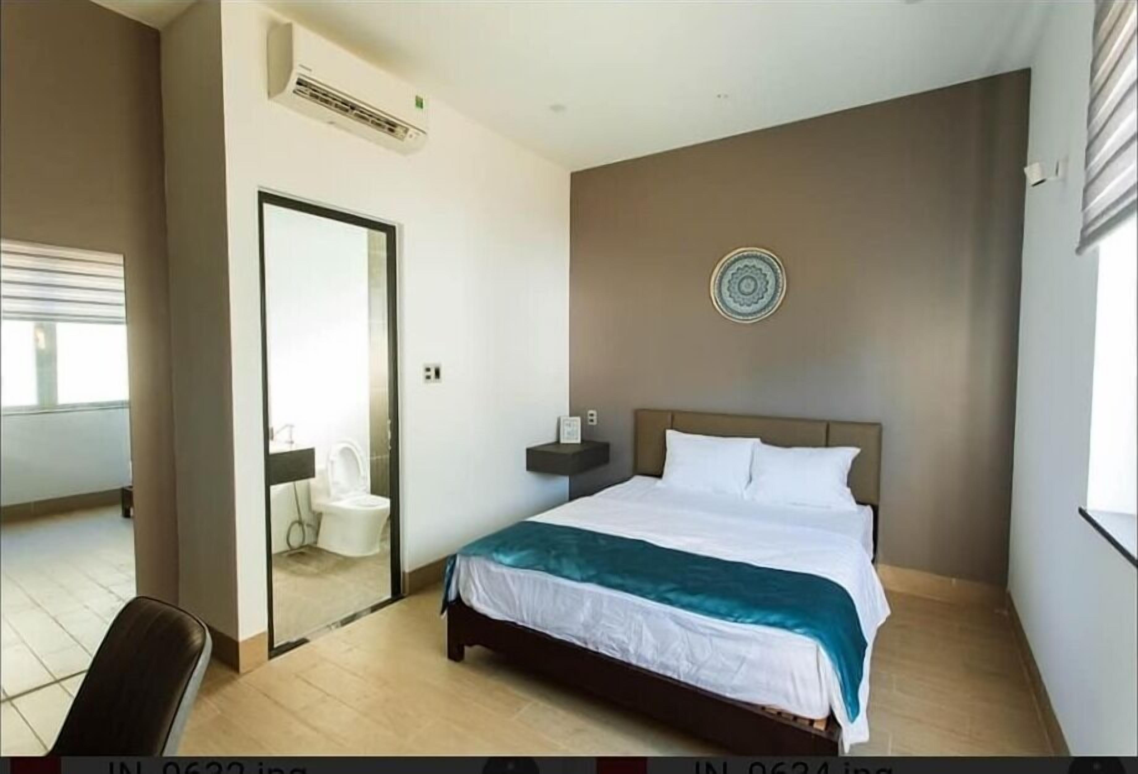 A modern hotel room with a bed, a bedside table, a mirror, and a view of the bathroom.