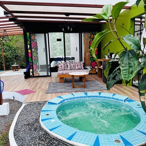 Relax in the hot tub surrounded by lush greenery and a shaded deck with a bench.