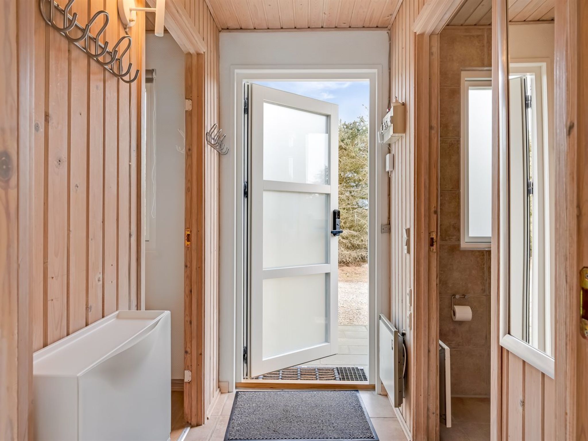 A wooden interior hallway with a door leading outside, a small step, and a doormat.