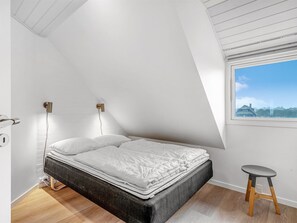 Ein Schlafzimmer mit Bett, Fenster und einem kleinen Hocker.