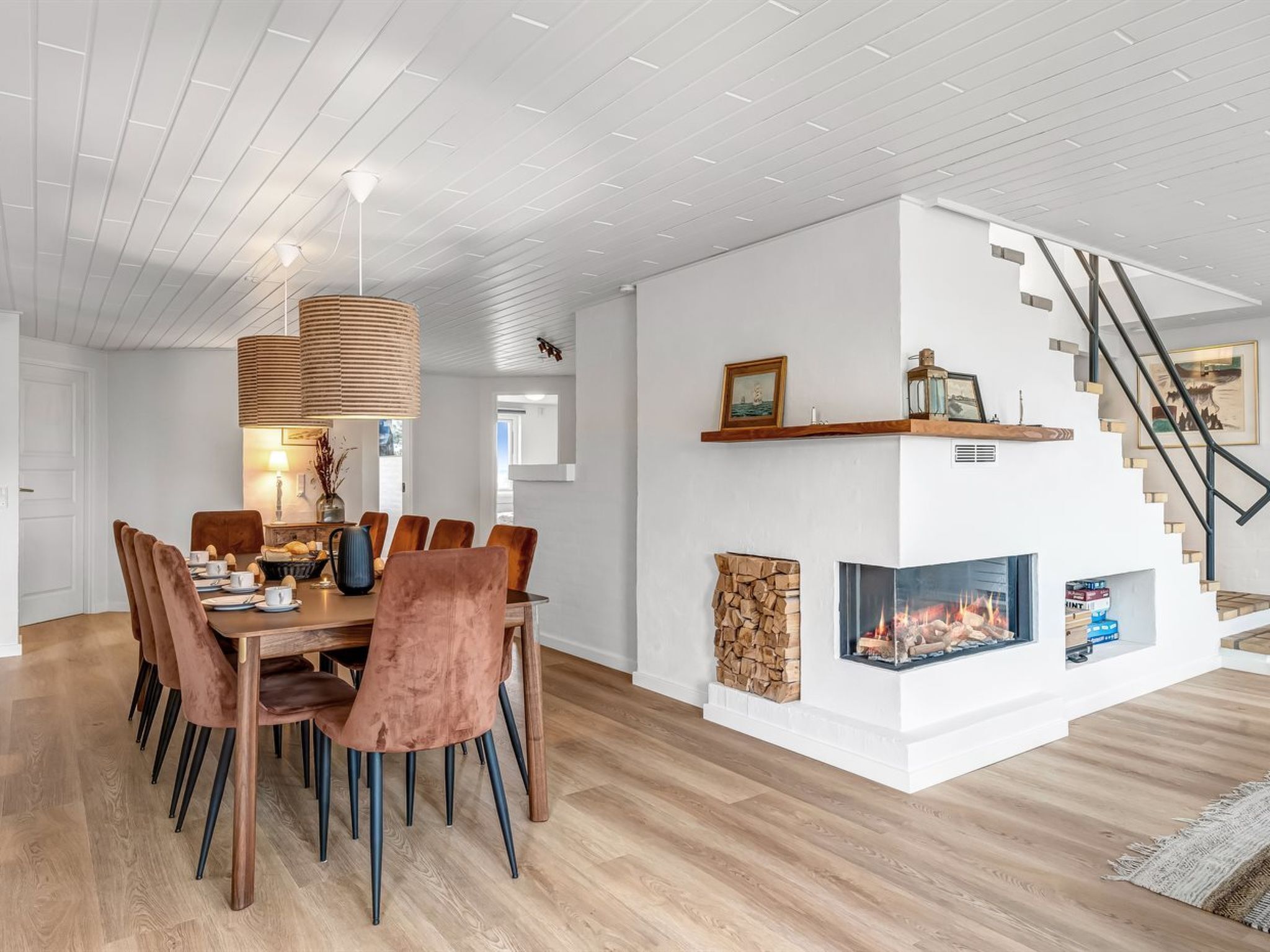 Un comedor moderno con una mesa y sillas de madera, una lámpara colgante y una chimenea con revestimiento de piedra.