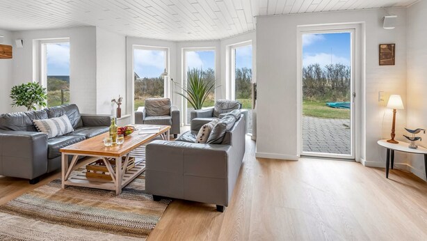 Ein geräumiges Wohnzimmer mit Holzbalkendecke, großen Fenstern und Blick ins Freie.