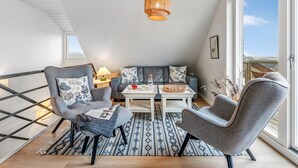 Ein modernes Schlafzimmer im Loft-Stil mit schrägem Dach, einem großen Fenster, einem Essbereich mit Tisch und Stühlen und einer gemütlichen Sitzecke mit Sofa und Sesseln.