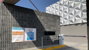 A hotel entrance with a brick wall and a geometric white facade. There are signs indicating room rates and welcome messages.
