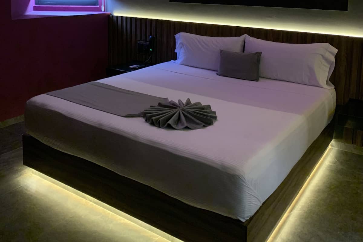 Un dormitorio moderno con una cama grande, un televisor montado en la pared y una lámpara en el techo.