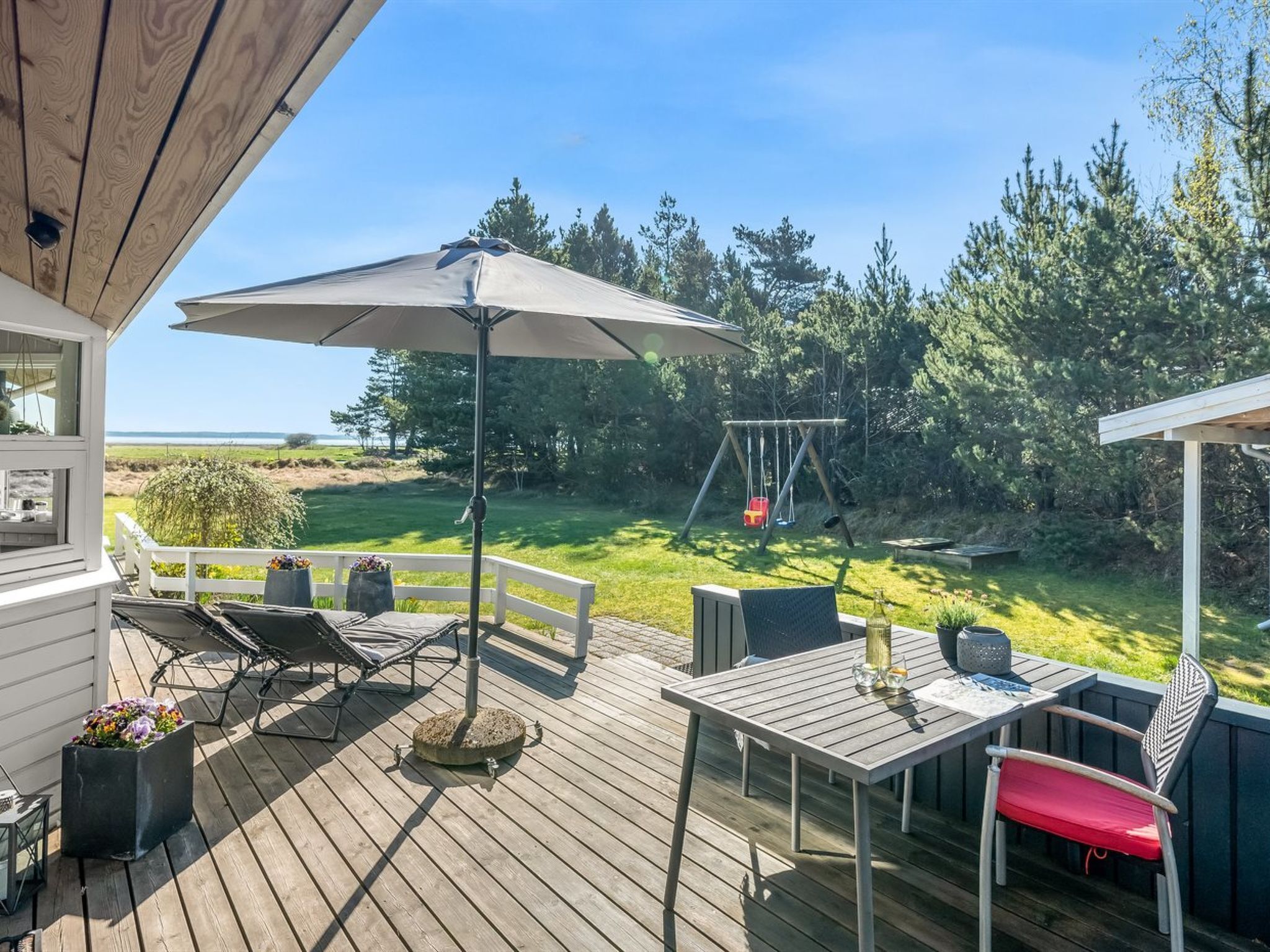 A wooden deck with outdoor furniture, a swing set, and a view of the landscape.
