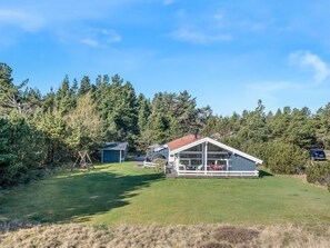 Une maison dotée d’une grande terrasse, d’un garage et d’une cour entourée d’arbres.