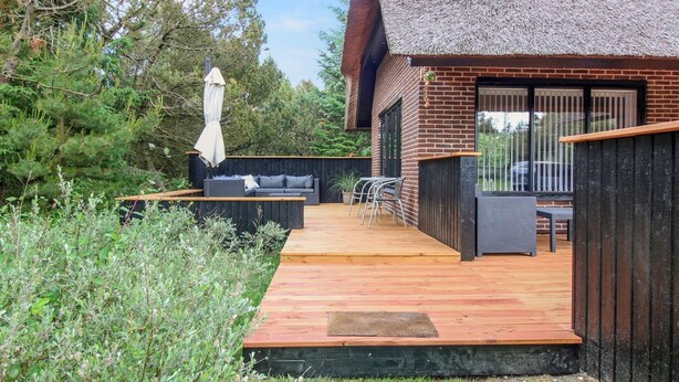 A modern house with a thatched roof, a wooden deck, and a seating area with a sofa and chairs.