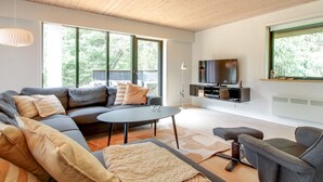 A modern living room with a sectional sofa, a round coffee table, and a TV on a black stand.