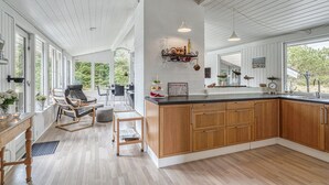 Et rummeligt køkken med træskabe, en stor ø og et spiseområde med stol og bord.
