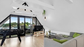 Moderni loft-tyylinen asunto, jossa on suuri ikkuna, harmaa sohva, musta televisio ja puulattia.