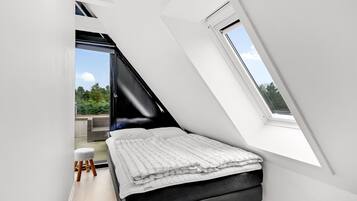 Une chambre avec un plafond en pente, un lit, un petit tabouret et une fenêtre.