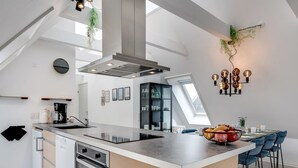 Moderni keittiö, jossa on keskeinen saareke, sisäänrakennettu uuni ja ruokailutila, jossa on siniset tuolit.